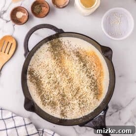 Velvety Chicken Alfredo Pot Pie 9 Cheese and seasonings being mixed into the creamy sauce in a cast iron skillet.