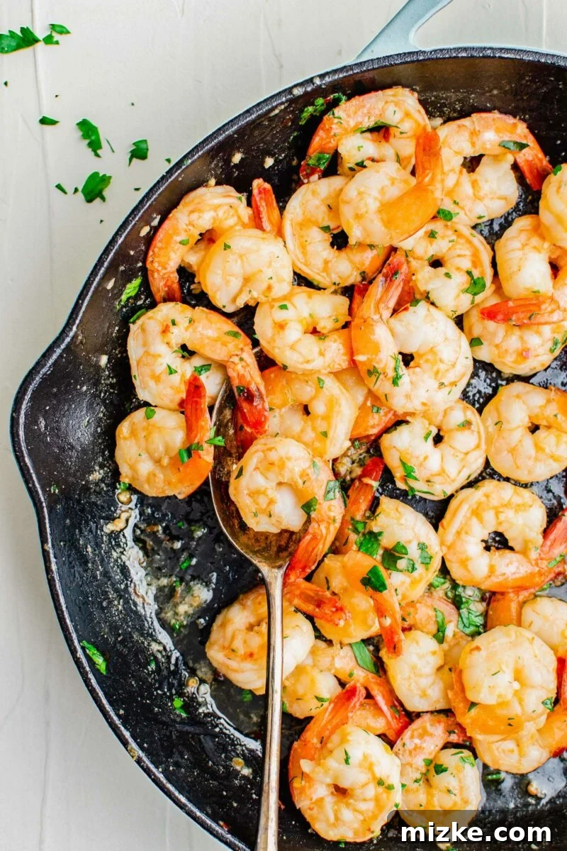 Sizzling Lemon Garlic Shrimp 2 Cooked shrimp are being scooped from a black skillet with a metal spoon.