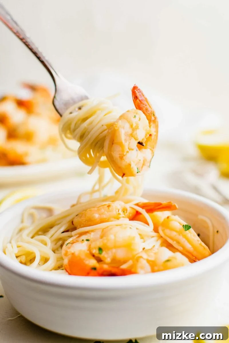 Sizzling Lemon Garlic Shrimp 6 A fork is lifting a bite sized portion of noodles and a single cooked shrimp from a white bowl.