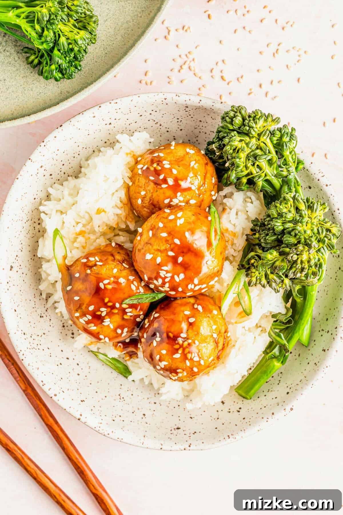 Oven-baked teriyaki tofu meatballs, crispy and coated in a sweet-and-savory sauce. A favorite for tofu lovers and skeptics alike! Bowl of rice and steamed broccoli topped with teriyaki tofu meatballs, garnished with sesame seeds and green onions.