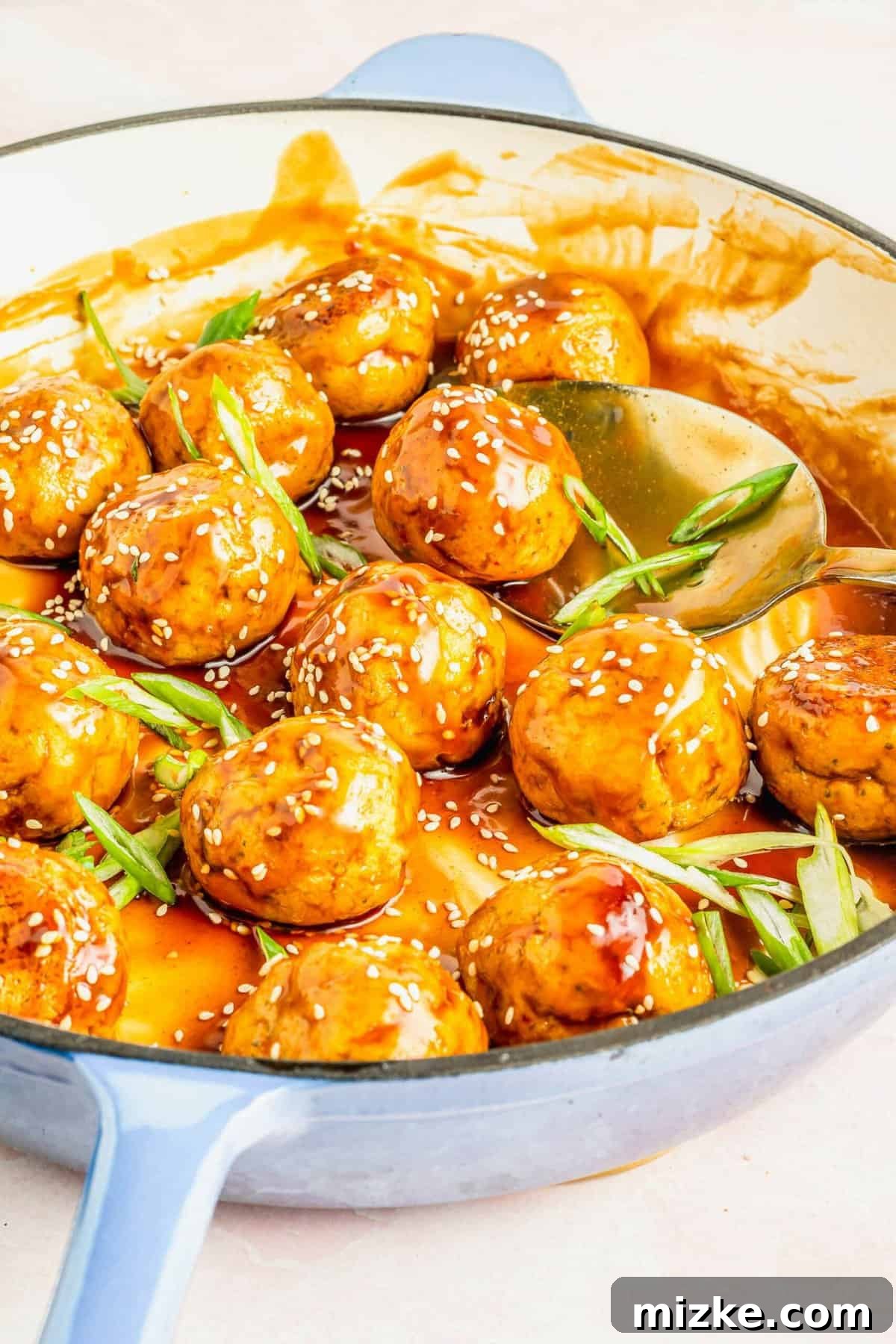 Saucy and delicious: teriyaki tofu meatballs finished in the skillet. Teriyaki tofu meatballs generously coated in sauce, garnished with fresh scallions and sesame seeds, served in an enamel skillet.