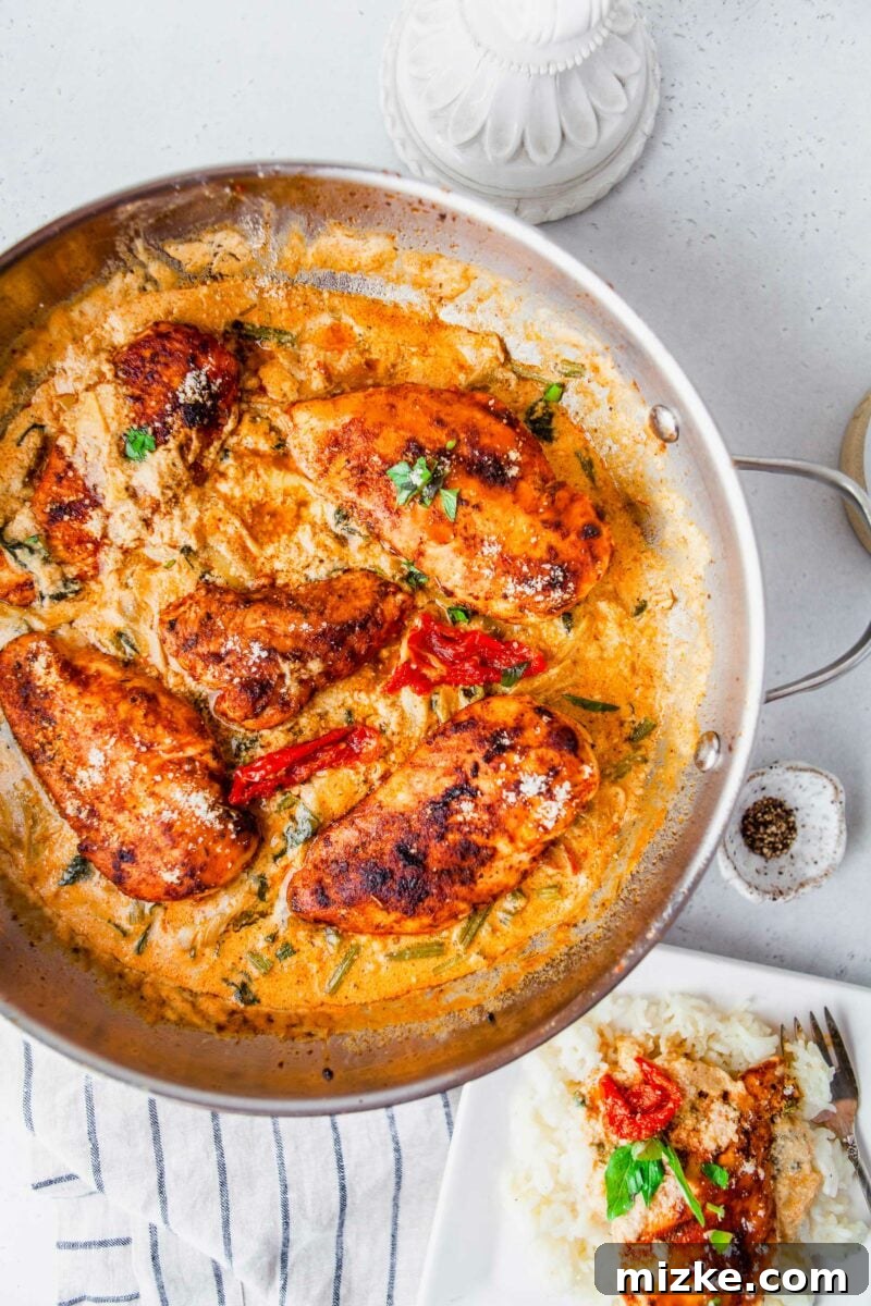 Velvety Tuscan Chicken 5 A silver skillet filled with golden chicken breasts swimming in rich, orange-hued creamy Tuscan sauce, ready to be served.