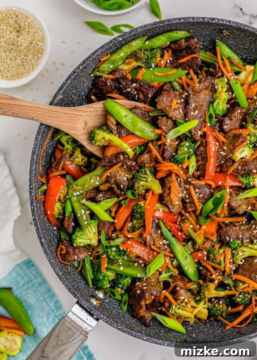 Sizzling Beef Stir Fry 2 A wooden spoon is placed in a large skillet filled with perfectly cooked beef stir fry, garnished with sesame seeds, ready to be served.