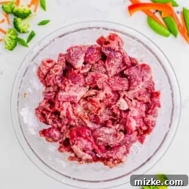 Sliced beef marinating in a clear bowl with cornstarch and soy sauce, ready for stir frying.