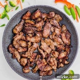 Browned slices of beef searing in a nonstick skillet, preparing for the stir fry.