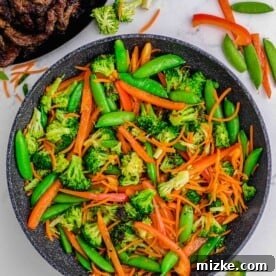 Broccoli, snow peas, carrots, and red bell peppers cooking in a hot skillet, retaining their vibrant colors.