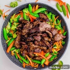 Cooked beef slices being added back to the skillet with the stir-fried vegetables.
