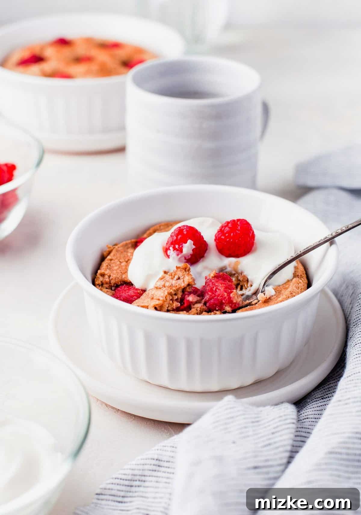 Raspberry Oatmeal Bake 3 A close-up view of raspberry baked oatmeal in a white bowl, elegantly garnished with a spoonful of Greek yogurt and fresh raspberries, highlighting its soft, inviting texture.