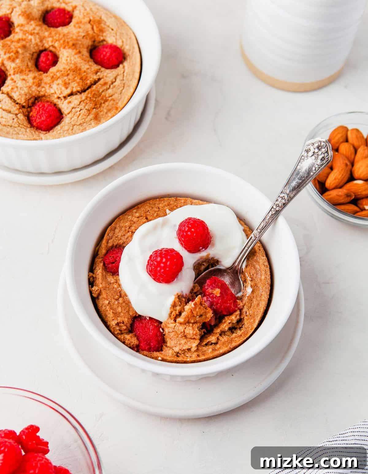 Raspberry Oatmeal Bake 6 Elegantly presented raspberry baked oatmeal in a white bowl with a spoon, generously garnished with creamy Greek yogurt and an assortment of fresh berries, ready to be enjoyed as a wholesome meal.
