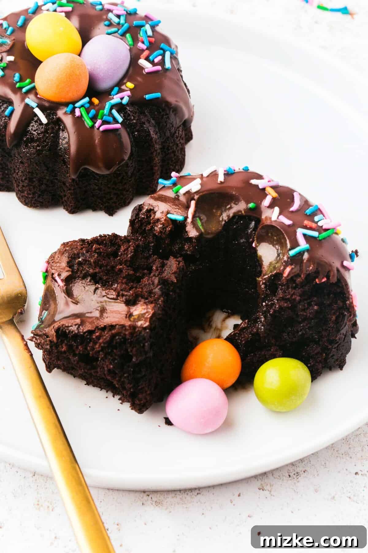 A mini bundt cake has been meticulously cut in half, showcasing its moist chocolate interior and the rich chocolate ganache that elegantly drizzles through its central cavity.