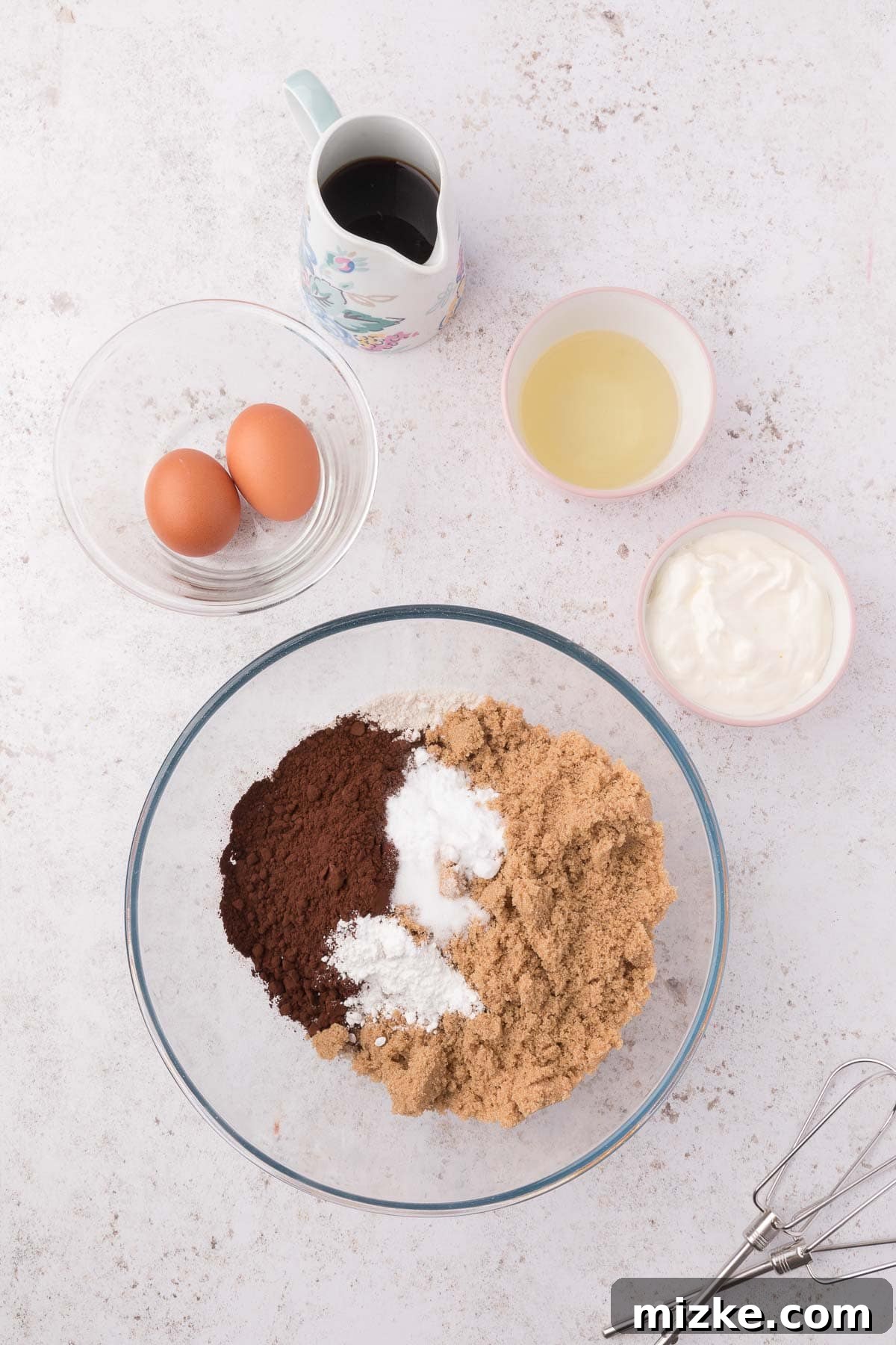 A glass bowl holds the dry ingredients for mini bundt cakes, including flour, cocoa powder, and sugar, ready for mixing.