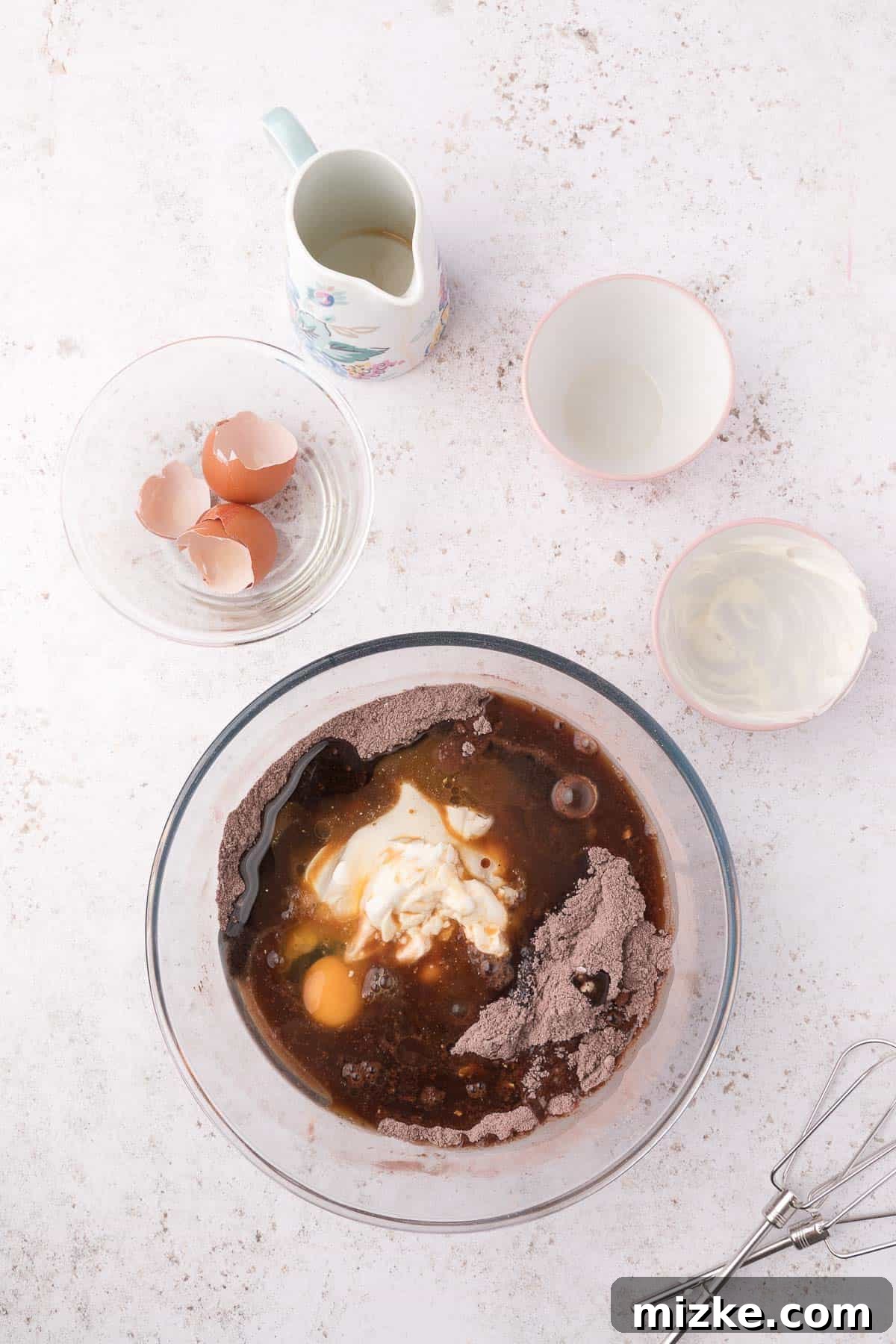 Two glass bowls, one with dry ingredients for mini bundt cakes and another with wet ingredients, poised to be combined.