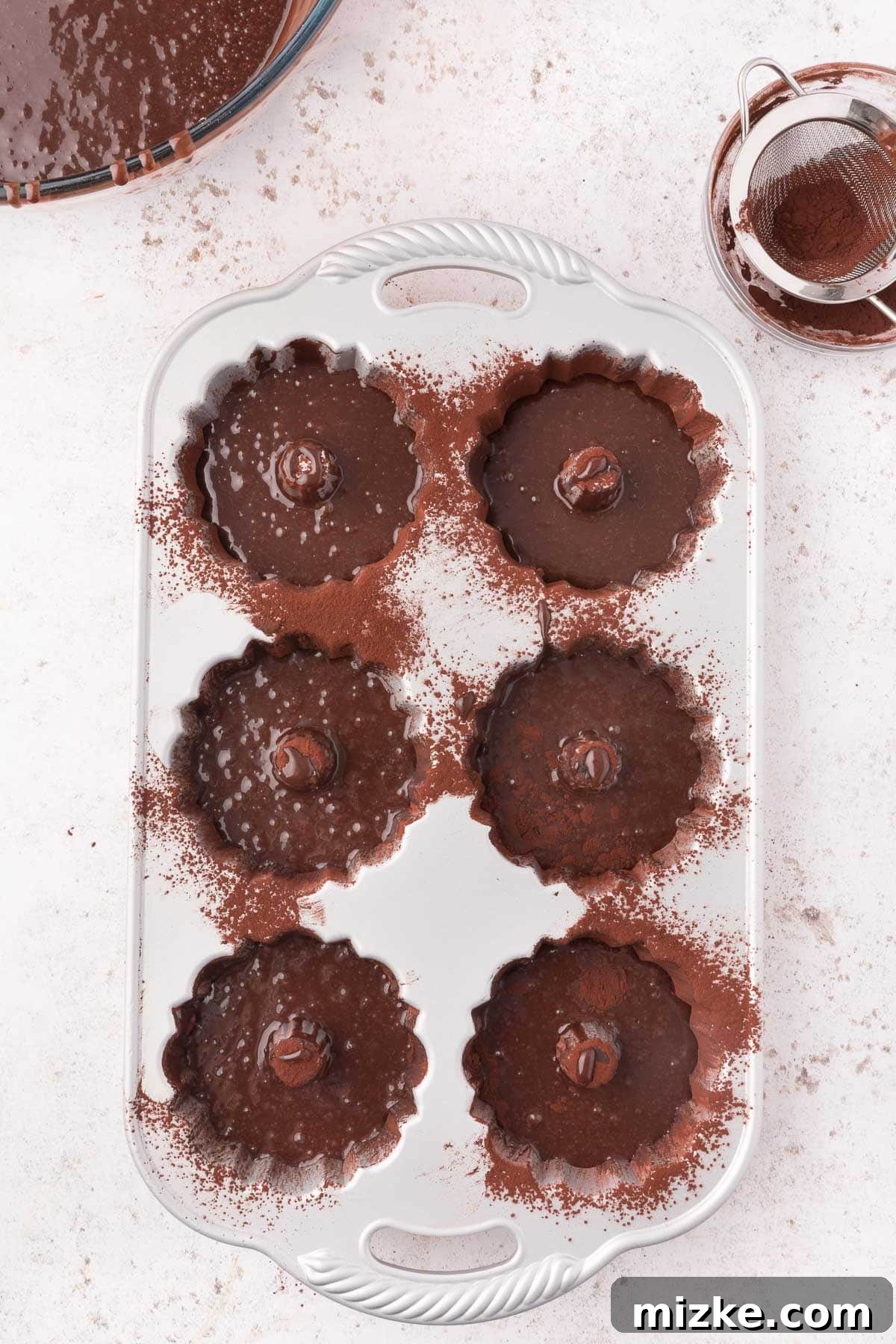 Mini bundt pans are precisely filled with rich chocolate batter, illustrating the optimal fill level before baking.