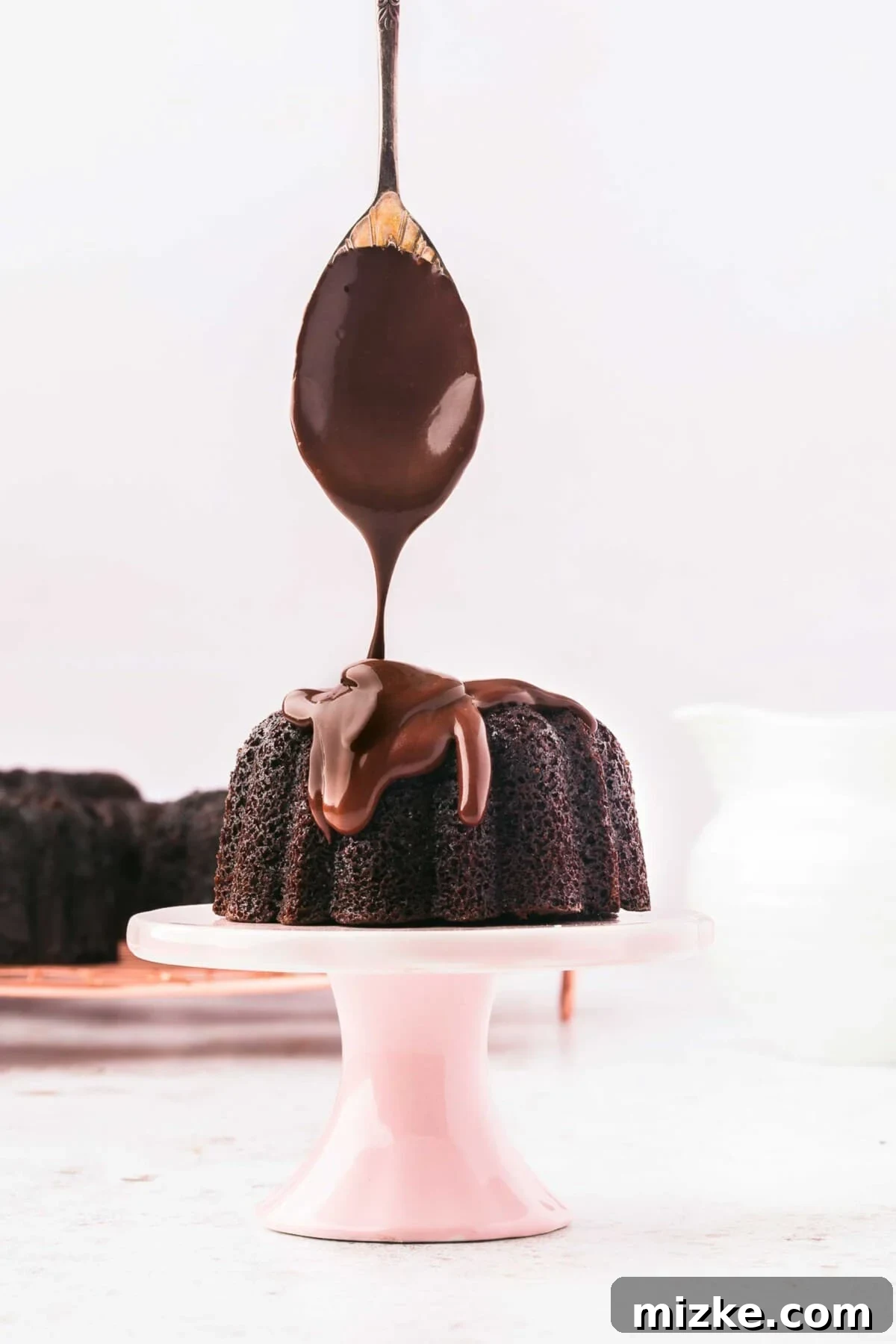 A spoon meticulously drizzles rich chocolate ganache onto a freshly baked chocolate bundt cake, creating a perfect glaze.