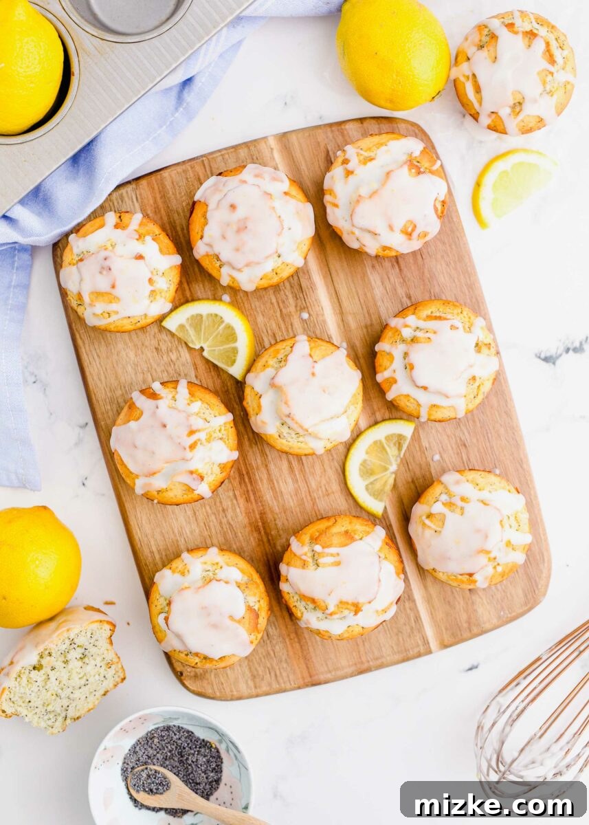 Zesty Lemon Poppy Seed Muffins 2 Nine glazed lemon poppyseed muffins are placed on a wooden board with two lemon slices, highlighting their golden tops and smooth glaze.