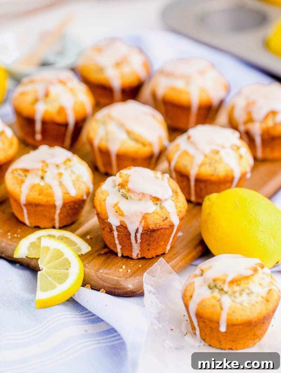 Zesty Lemon Poppy Seed Muffins 3 A batch of glazed lemon poppyseed muffins is artfully arranged on a wooden serving board, surrounded by whole lemons and extra muffins for a plentiful display.