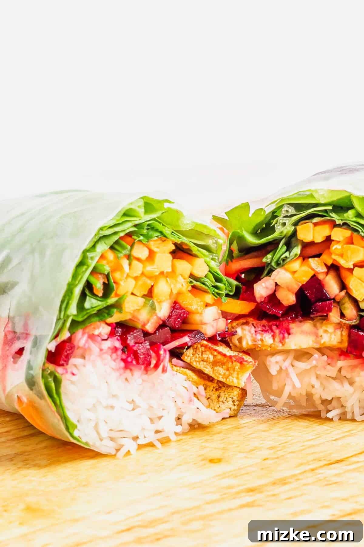 Vegan Summer Wraps 3 A perfectly rolled tofu summer roll, sliced in half to reveal layers of colorful julienned vegetables, crispy tofu strips, and delicate rice noodles nestled inside the translucent rice paper wrapper.