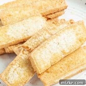 Crispy golden-brown tofu strips cooling on a speckled plate after frying.