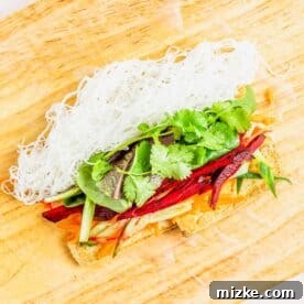 Ingredients for a tofu summer roll meticulously arranged on a translucent rice paper wrapper on a wooden cutting board, ready for rolling.