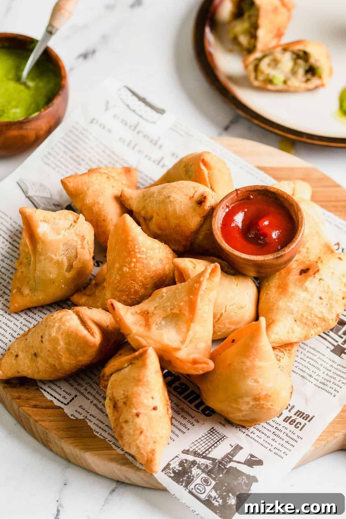 Golden Crispy Vegetable Samosas 6 Three golden-brown vegetable samosas arranged on a sheet of newspaper with a small bowl of dipping sauce beside them.