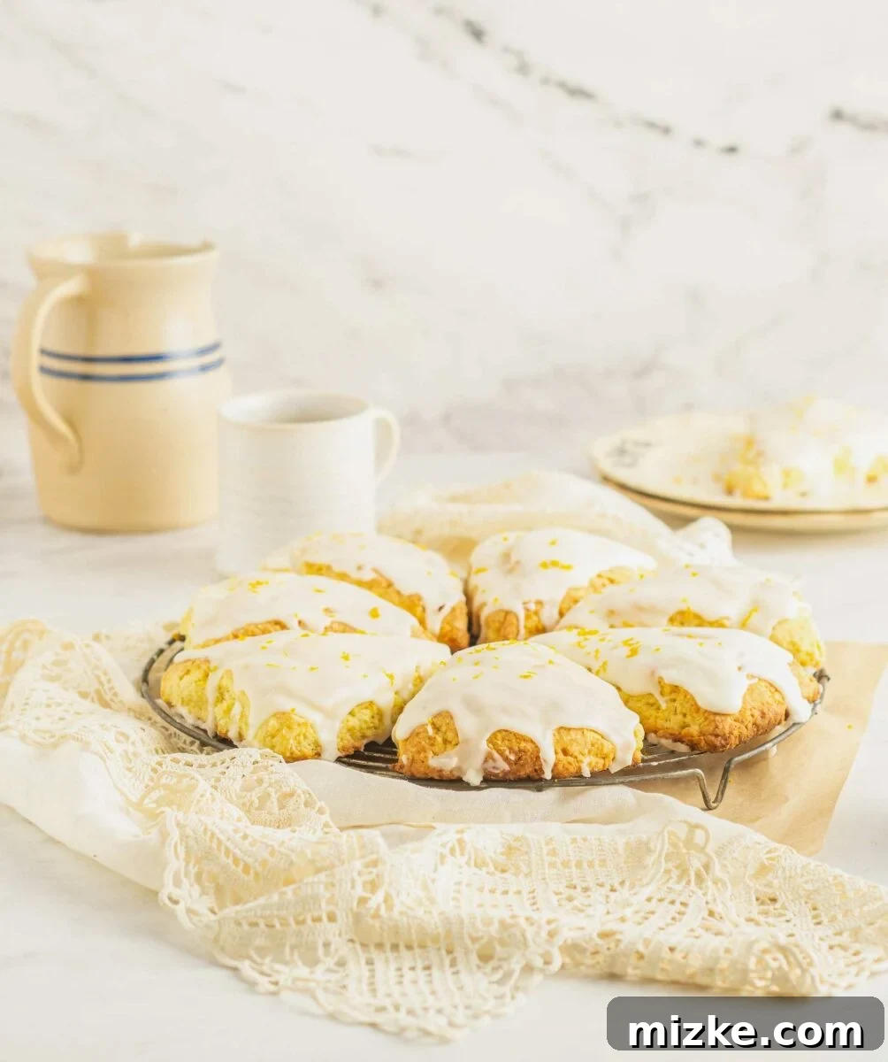 A batch of homemade orange scones is presented on a cooling rack on top of a white lace tablecloth. The scones are golden brown with a glistening orange glaze.