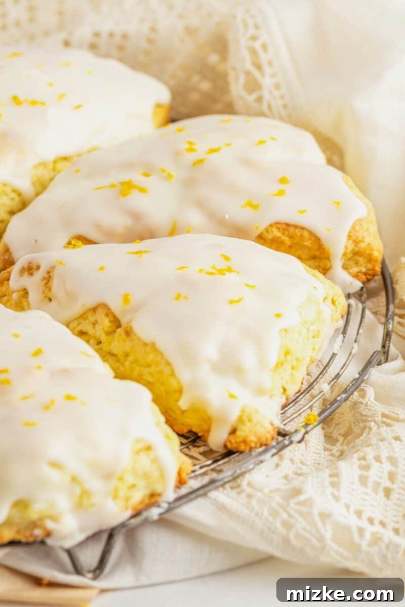 Glazed orange scones are neatly arranged on a wire cooling rack, garnished with delicate strands of fresh orange zest for an extra touch of flavor and visual appeal.