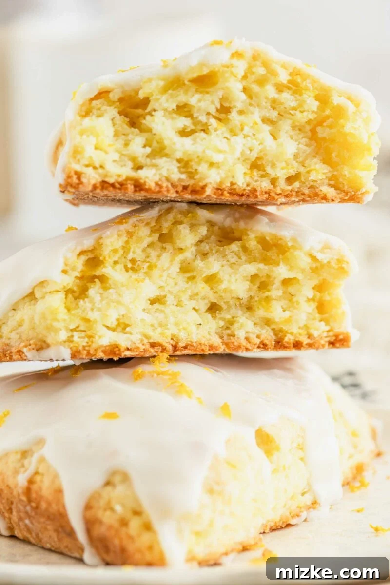Several golden-brown orange scones are stacked on top of one another, showcasing their tender crumb. One scone has been split in half to reveal its perfectly cooked interior.