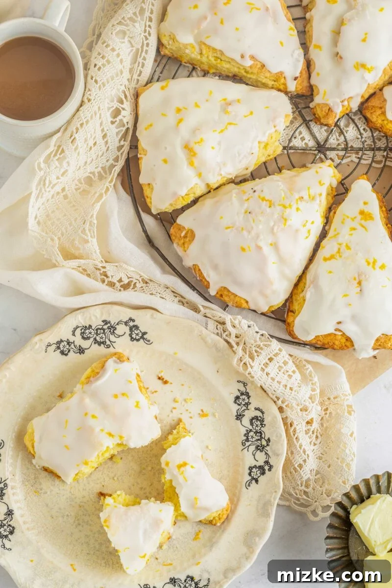 A selection of freshly baked orange scones, some glazed, are presented on a cooling rack next to a single glazed scone plated on a small white dish, ready to be enjoyed.