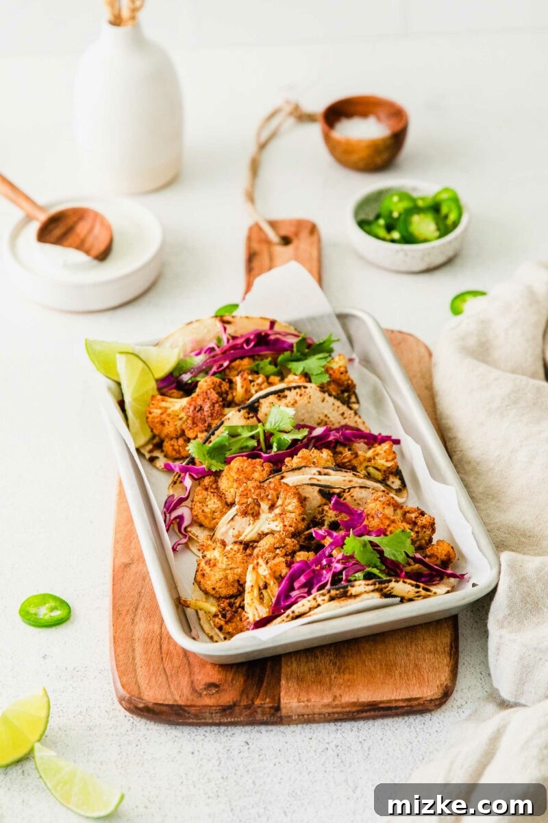 Crispy Spiced Vegan Cauliflower Tacos 3 Two metal trays of three vegan cauliflower tacos each, artfully arranged on a rustic wooden cutting board, garnished with cilantro, ready to be served and enjoyed.