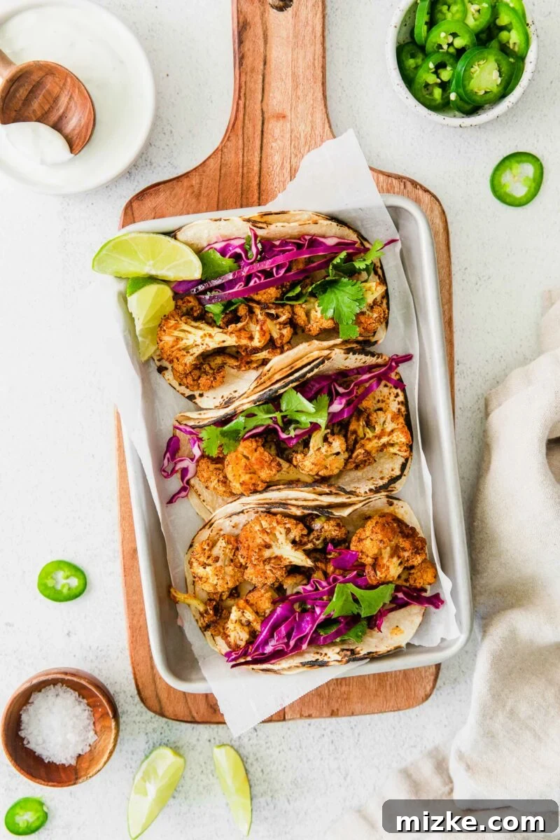 Crispy Spiced Vegan Cauliflower Tacos 4 Close-up of three vegan cauliflower tacos on a metal sheet, with fresh limes, kosher salt, and sliced jalapeños arranged beside them, ready for garnishing, highlighting the vibrant ingredients.