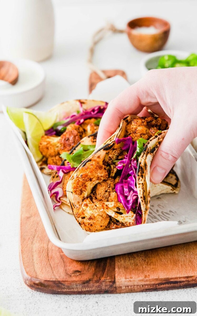 Crispy Spiced Vegan Cauliflower Tacos 6 A hand reaches in to grab one of the delicious vegan cauliflower tacos from a metal platter filled with several more, signifying the irresistible appeal of the dish.