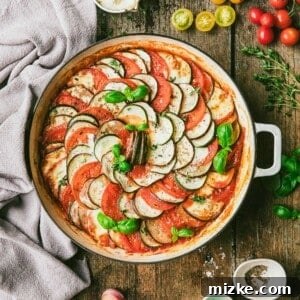 Ratatouille in round baking dish with ingredients and garnishes on tabletop