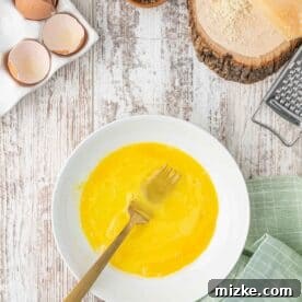 A shallow plate with eggs have been beaten with a metal gold fork