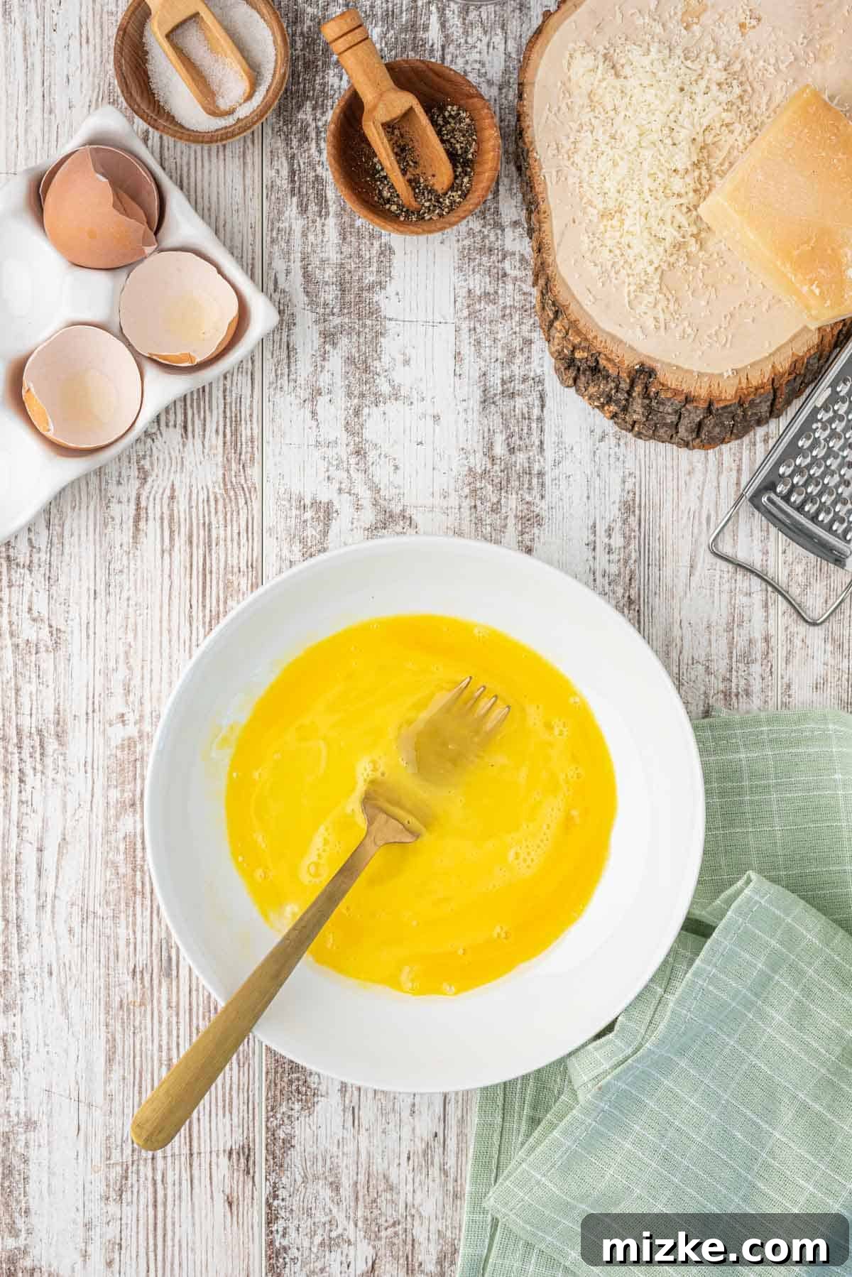 A shallow plate with eggs that have been beaten with a metal gold fork