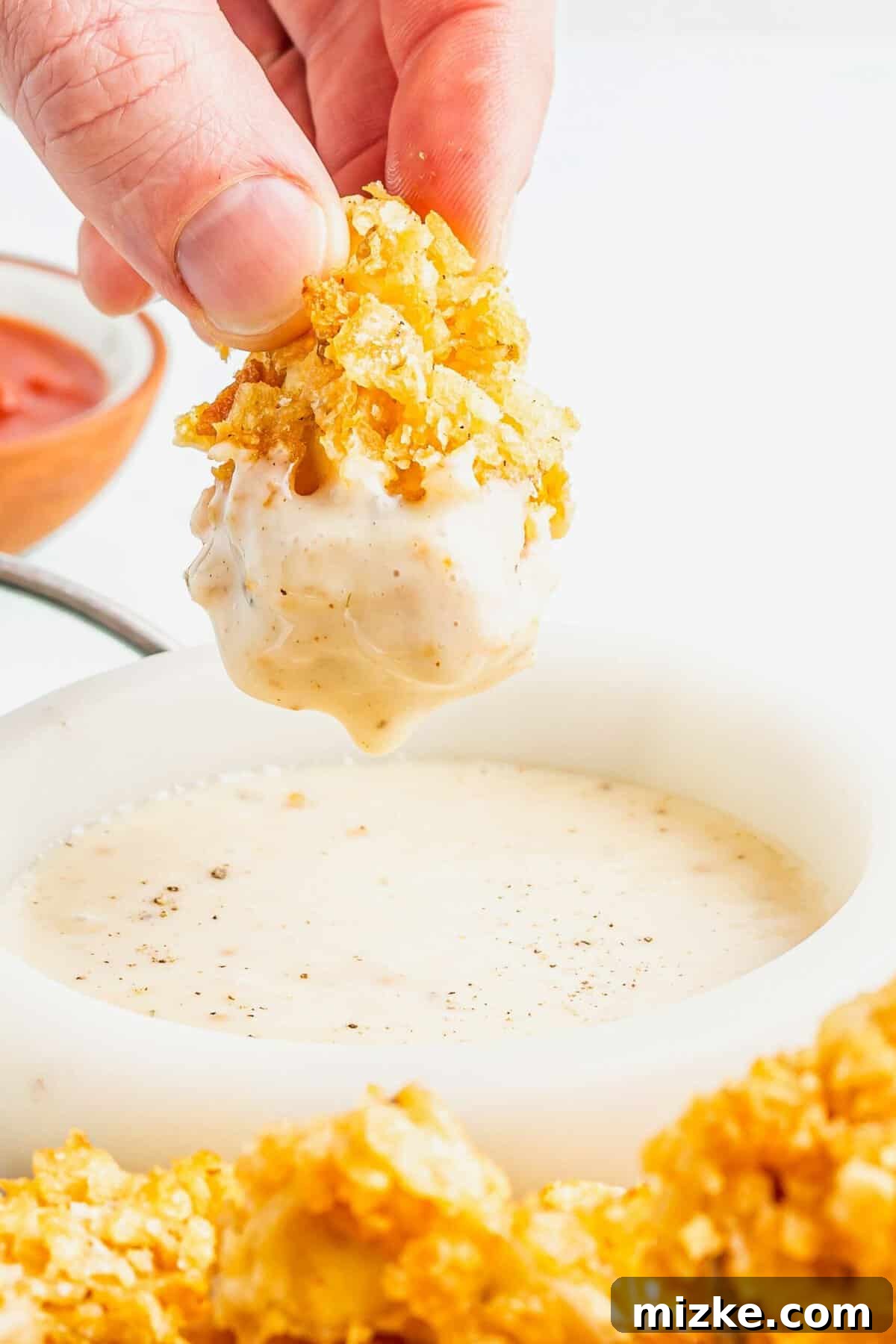 Crispy Tofu Poppers 5 A hand dipping a piece of crispy popcorn tofu into a bowl of creamy, light-colored sauce, showing the appealing texture of the tofu.