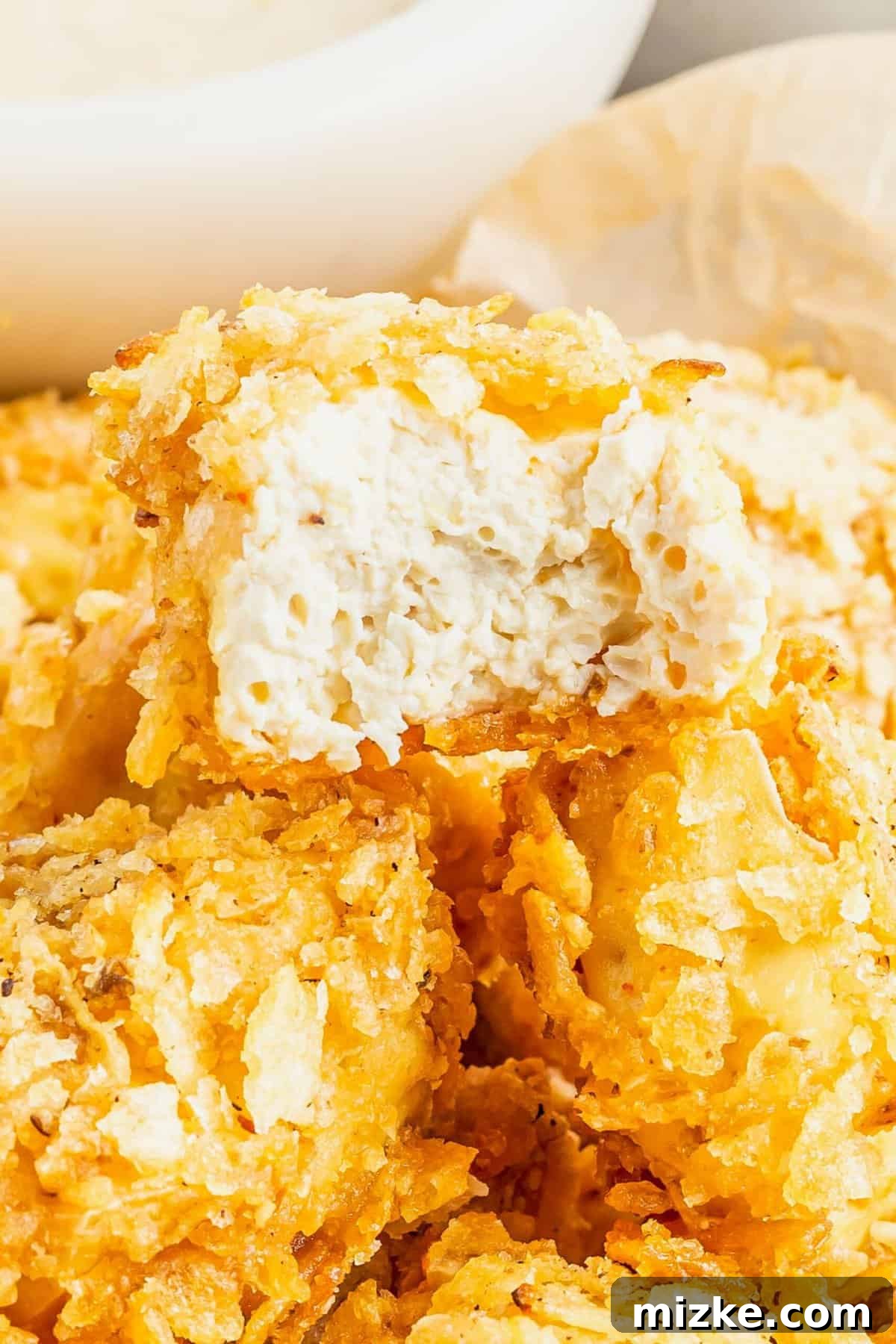 Crispy Tofu Poppers 6 A close-up view of a single piece of golden-brown popcorn tofu, with a small bite taken out to reveal the perfectly cooked, tender interior contrasted against the crispy potato chip coating.