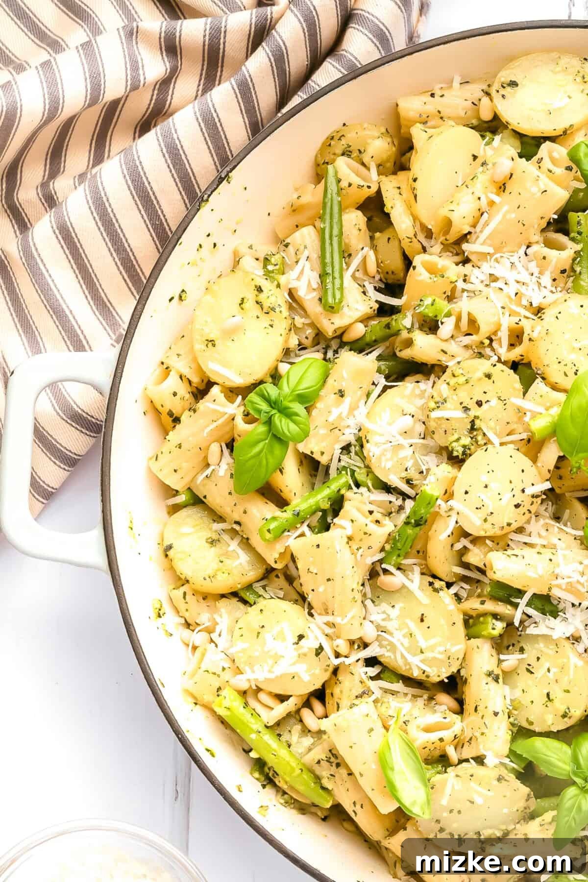 Rustic Pesto Pasta Trio 3 A large pot brimming with Pesto Pasta with Green Beans and Potatoes, artfully garnished with a sprinkle of pine nuts, grated Parmesan cheese, and fresh basil leaves, ready to be served.