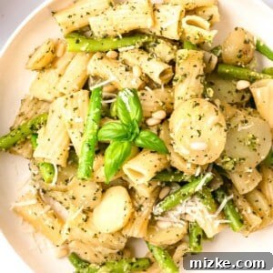 A vibrant close-up of pesto pasta garnished with pine nuts, parmesan, and basil on a white plate, highlighting the rich colors and textures.