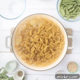 Rustic Pesto Pasta Trio 4 Rigatoni pasta added to boiling potatoes in a Dutch oven, submerged in vegetable broth, ensuring even cooking.