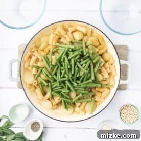 Rustic Pesto Pasta Trio 5 Fresh green beans added to sliced potatoes and pasta cooking in a Dutch oven, creating a colorful and balanced mix.