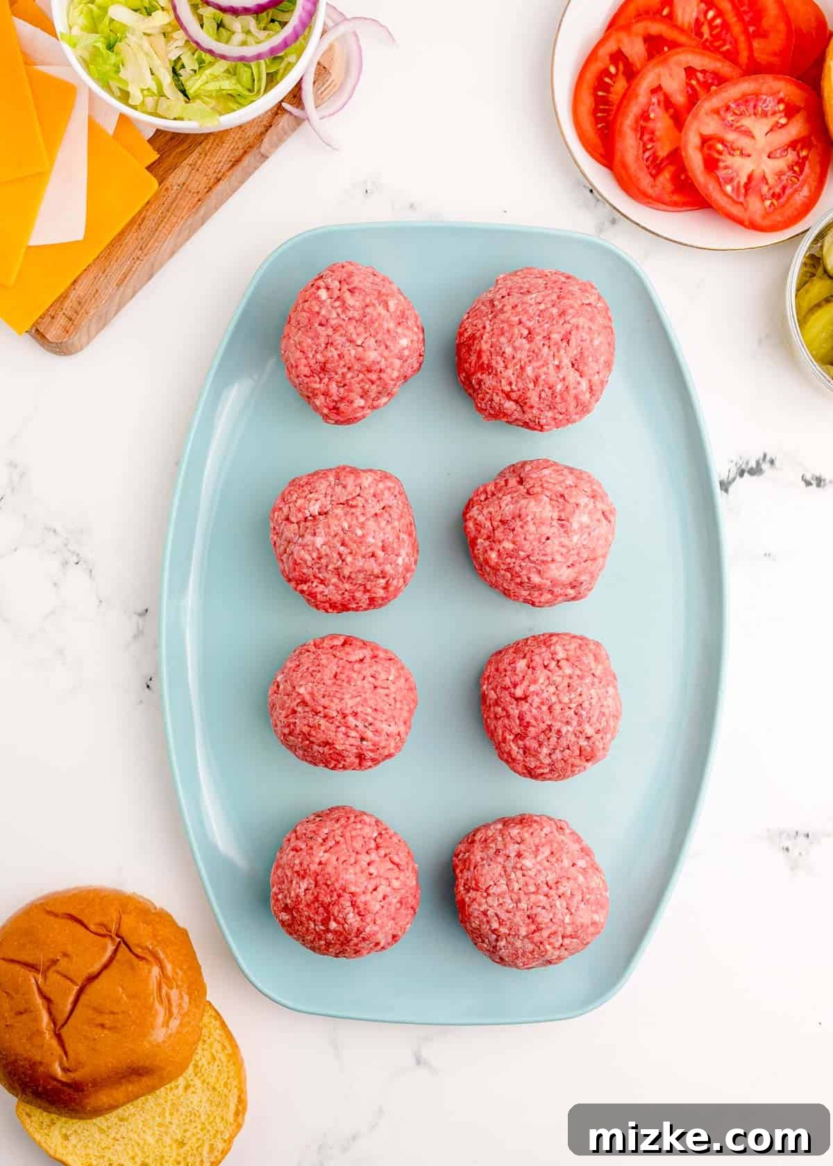 Eight evenly portioned balls of raw ground beef ready for smashing, resting on a blue plate.