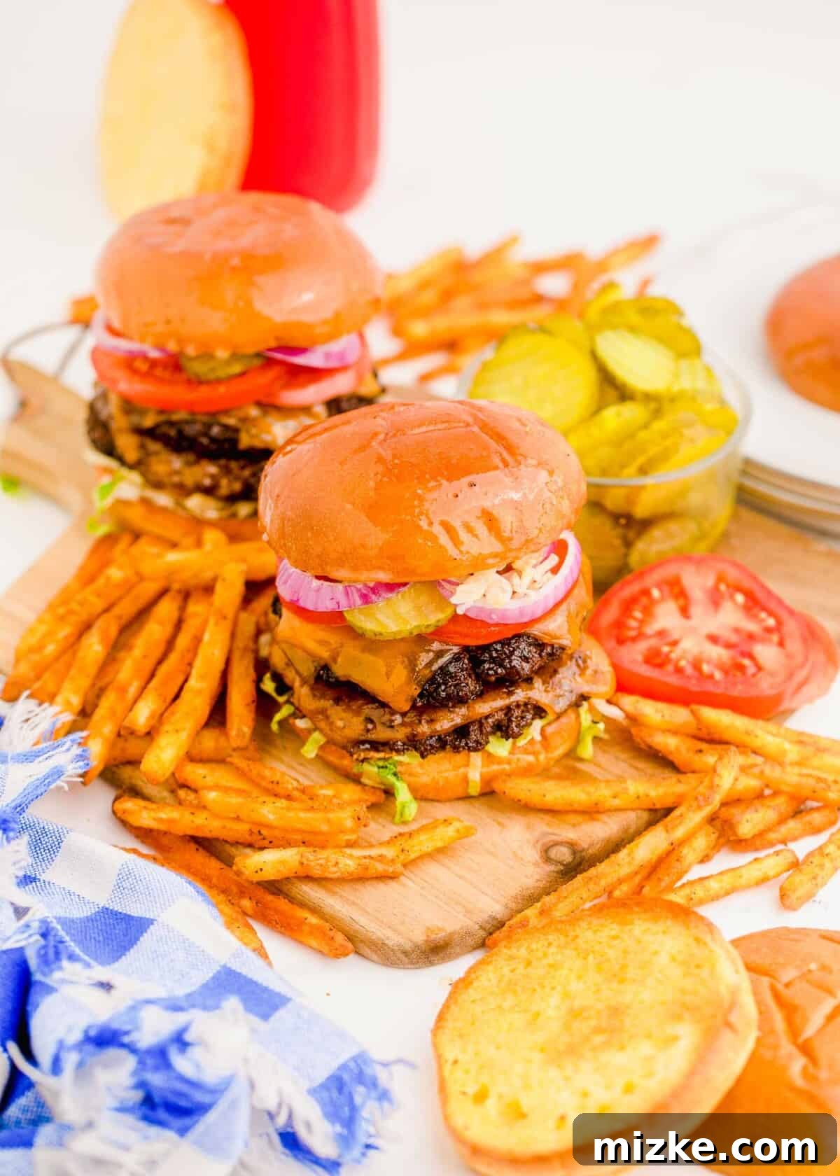 Two mouth-watering smash burgers garnished with fresh toppings like pickles, tomatoes, and lettuce, served alongside a pile of golden fries.