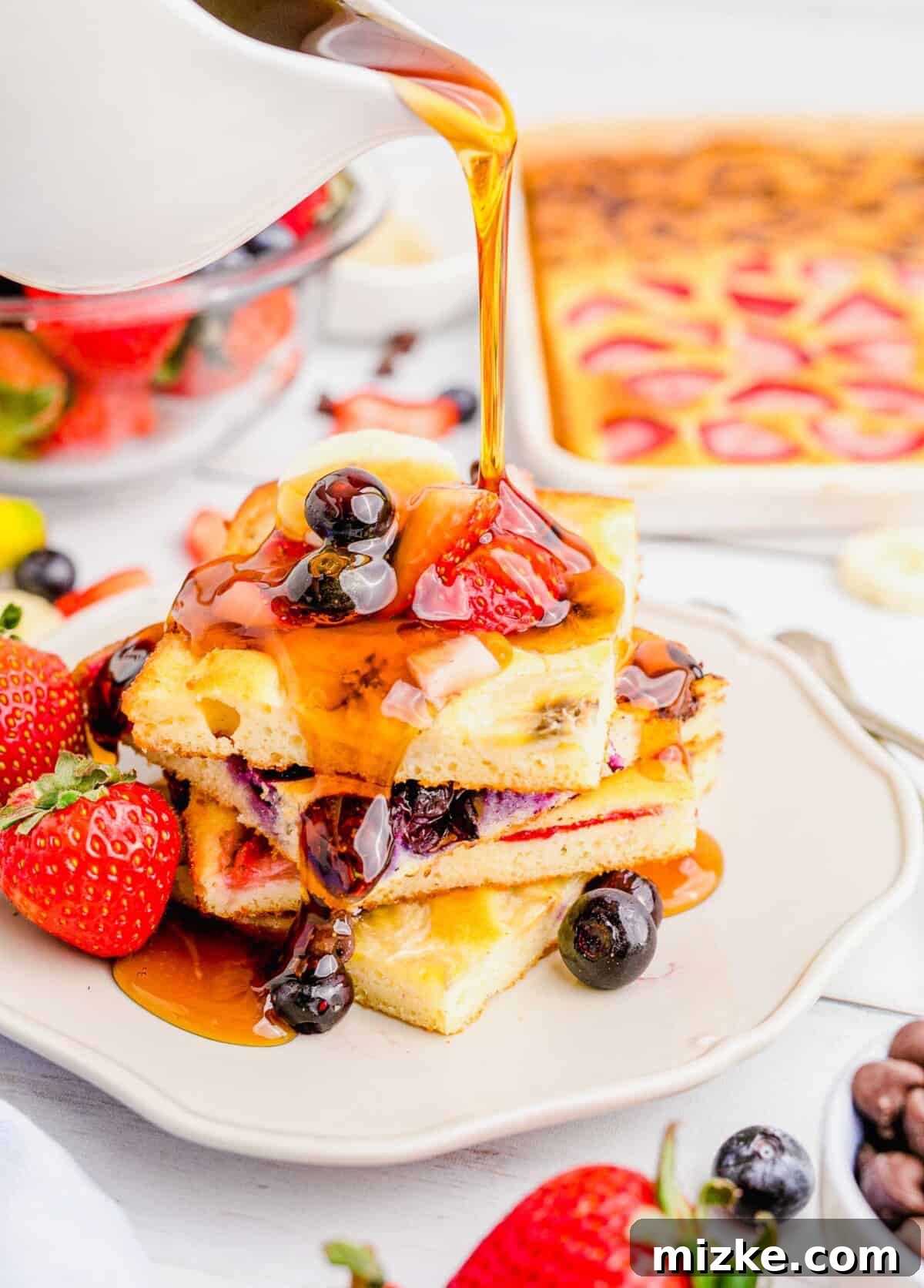 One-Pan Fruity Pancakes 12 Golden maple syrup being generously poured onto a perfectly stacked plate of square-cut fruity pancakes, ready to be enjoyed.