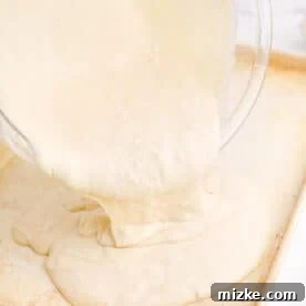 One-Pan Fruity Pancakes 19 Pancake batter being poured smoothly from a clear mixing bowl onto a greased metal sheet pan, ready for spreading.