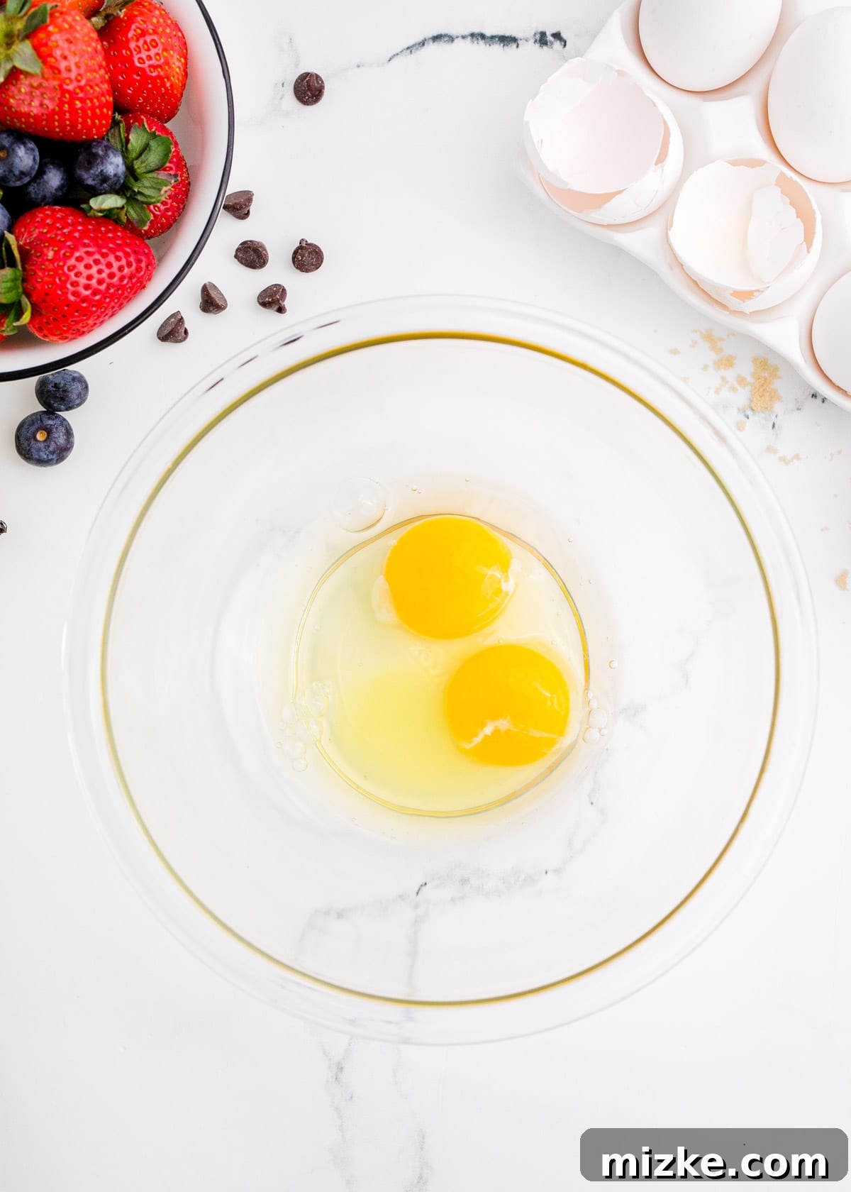 One-Pan Fruity Pancakes 6 Two fresh eggs in a clear bowl, with broken eggshells nearby, indicating preparation for a recipe.