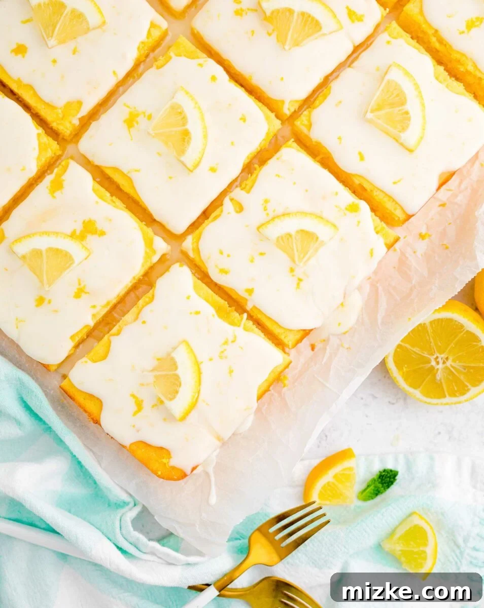 Lemon Bliss Sheet Cake 2 A beautifully sliced lemon sheet cake, garnished with fresh lemon wedges and delicate lemon zest, rests on a sheet of parchment paper, ready to be served.