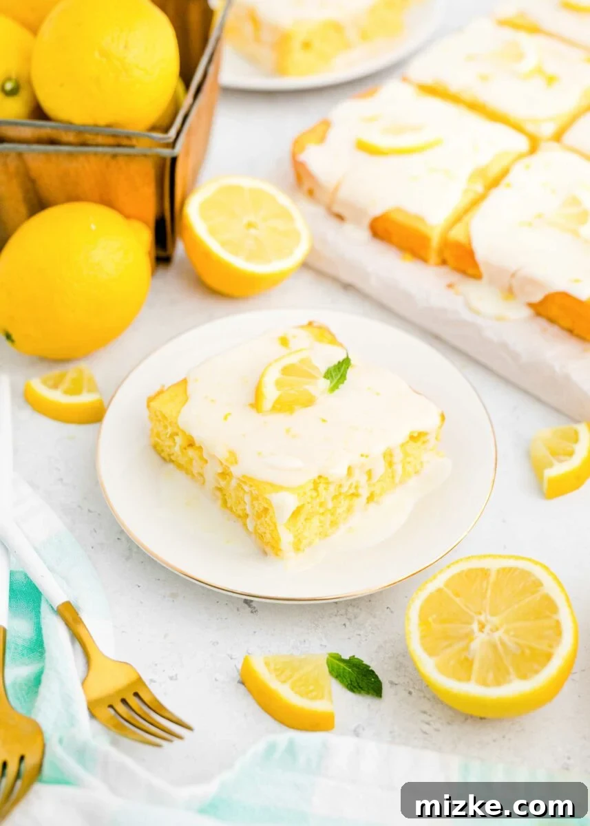 Lemon Bliss Sheet Cake 5 A refreshing lemon wedge and a silver fork are neatly positioned beside a white plate, which holds a single, inviting slice of lemon sheet cake, garnished for an appealing presentation.