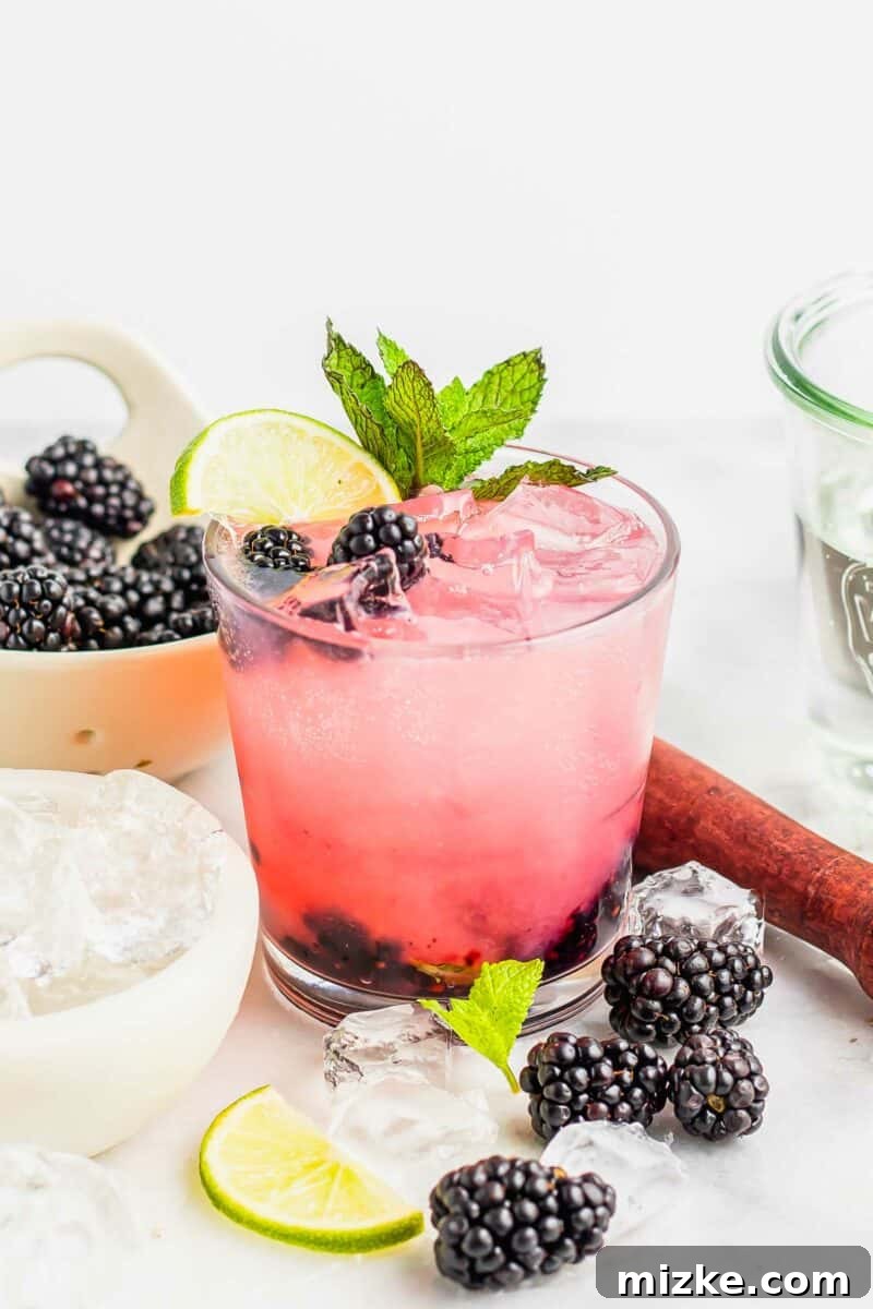 Velvet Blackberry Mint Mojito 4 Several blackberries and ice cubes are placed near a full glass of mojito.