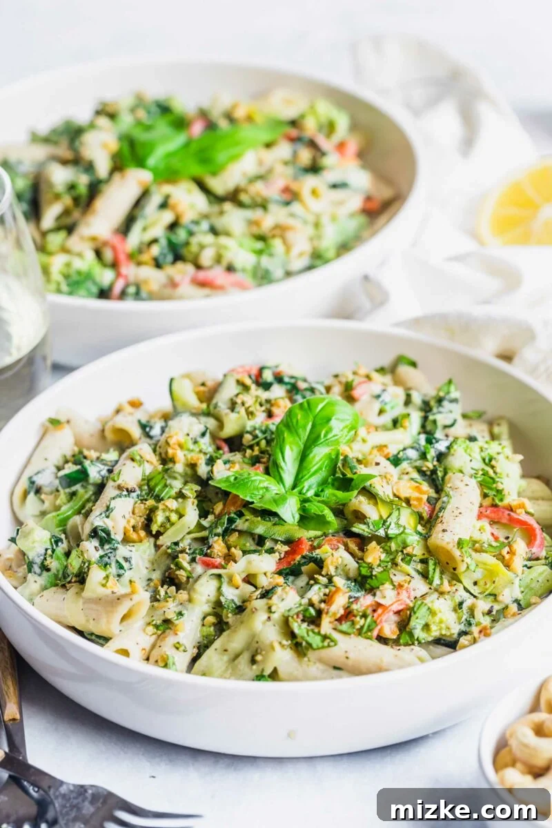 Velvet Cashew Basil Vegan Pasta 4 Two full bowls of creamy vegan basil cashew pasta, garnished with fresh basil and black pepper, are presented side-by-side on a clean white surface.
