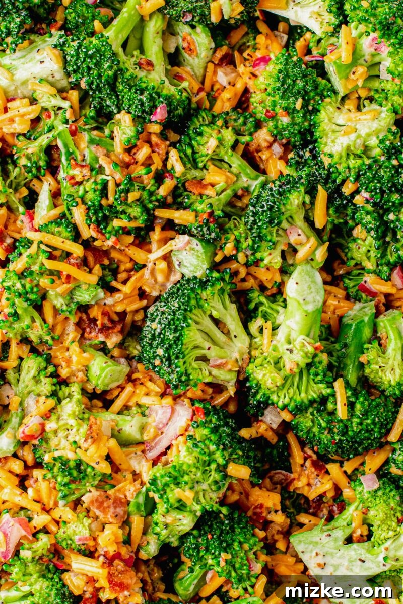Crisp Broccoli Delight 4 A vibrant mix of perfectly chopped fresh broccoli florets, golden shredded sharp cheddar cheese, crispy and savory bacon bits, and finely diced red onions are all tossed together in a large, pristine white mixing bowl. The ingredients are evenly distributed and awaiting the addition of the creamy dressing.
